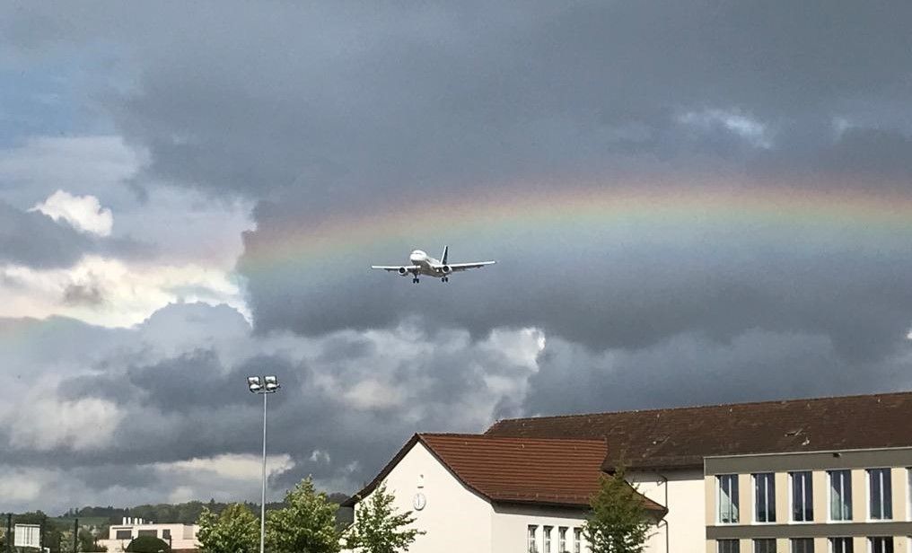 Ein Flugzeug fliegt über ein Gebäude mit einem Regenbogen im Hintergrund.