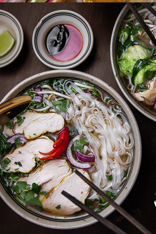 Schüsseln mit Pho, Nudeln, Hühnchen, Kräutern und Gewürzen, dunkelbrauner Tisch.