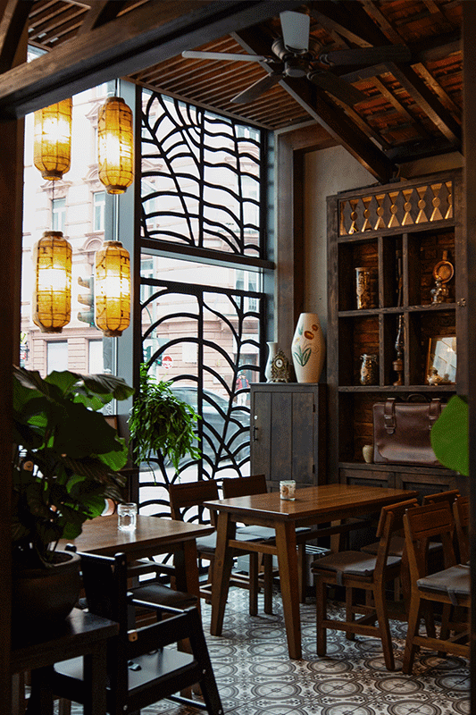 Gemütliches Restaurantinterieur mit Holzmöbeln, asiatischen Laternen, einem verzierten Fenster und einem dekorativen Regal.