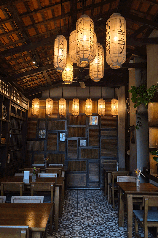 Restaurantinterieur mit Papierlaternen, Holzmöbeln und Fliesenboden.