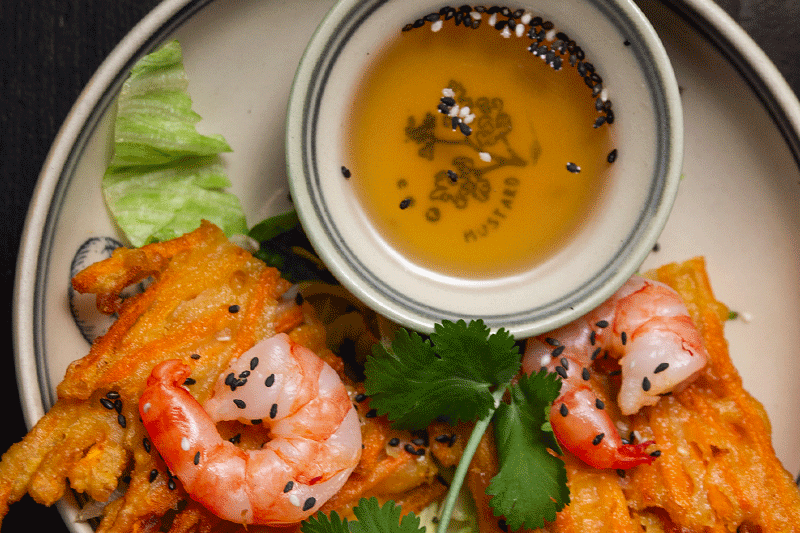 Krapfen mit Garnelen, serviert mit Dip-Sauce und garniert mit Koriander und Sesamsamen.