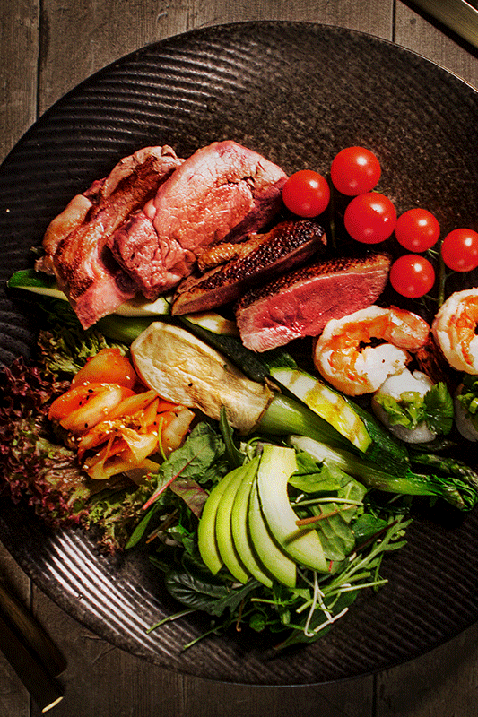 Teller mit geschnittener Entenbrust, Garnelen, Tomaten, Avocado und Gemüse.