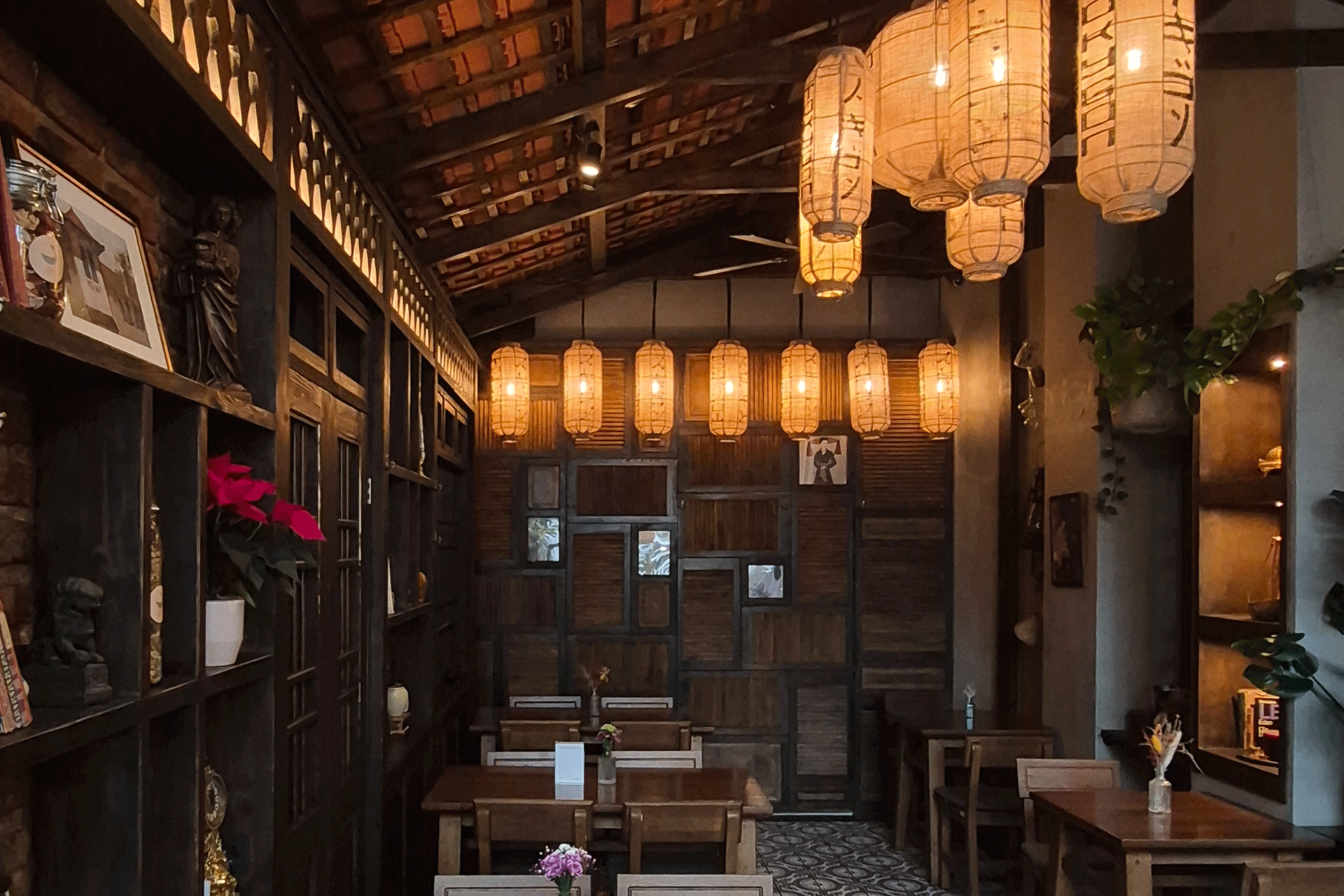 Gemütliches Café-Interieur mit Holzvertäfelung, hängenden Papierlaternen sowie kleinen Tischen und Stühlen.