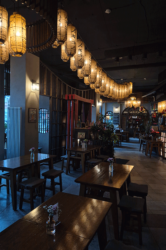 Das Interieur eines schwach beleuchteten japanischen Restaurants besteht aus Holztischen und -hockern, Papierlaternen an der Decke und dunklen Wänden.