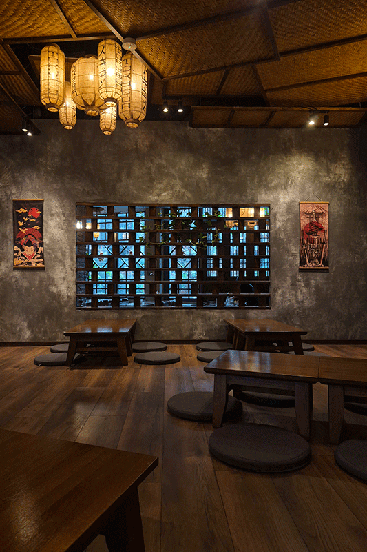 Interieur eines japanischen Teeraums. Niedrige Tische, Bodenkissen, Laternen hängen von der gewebten Decke. Großes Schaufenster im Hintergrund.