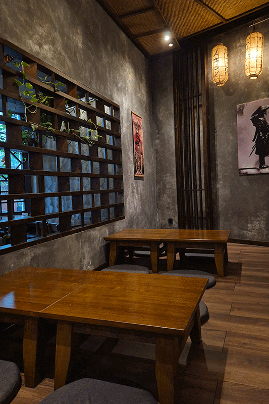 Restaurantinterieur im japanischen Stil mit Holztischen, dekorativer Wand und hängenden Laternen; freie Sitzplätze.