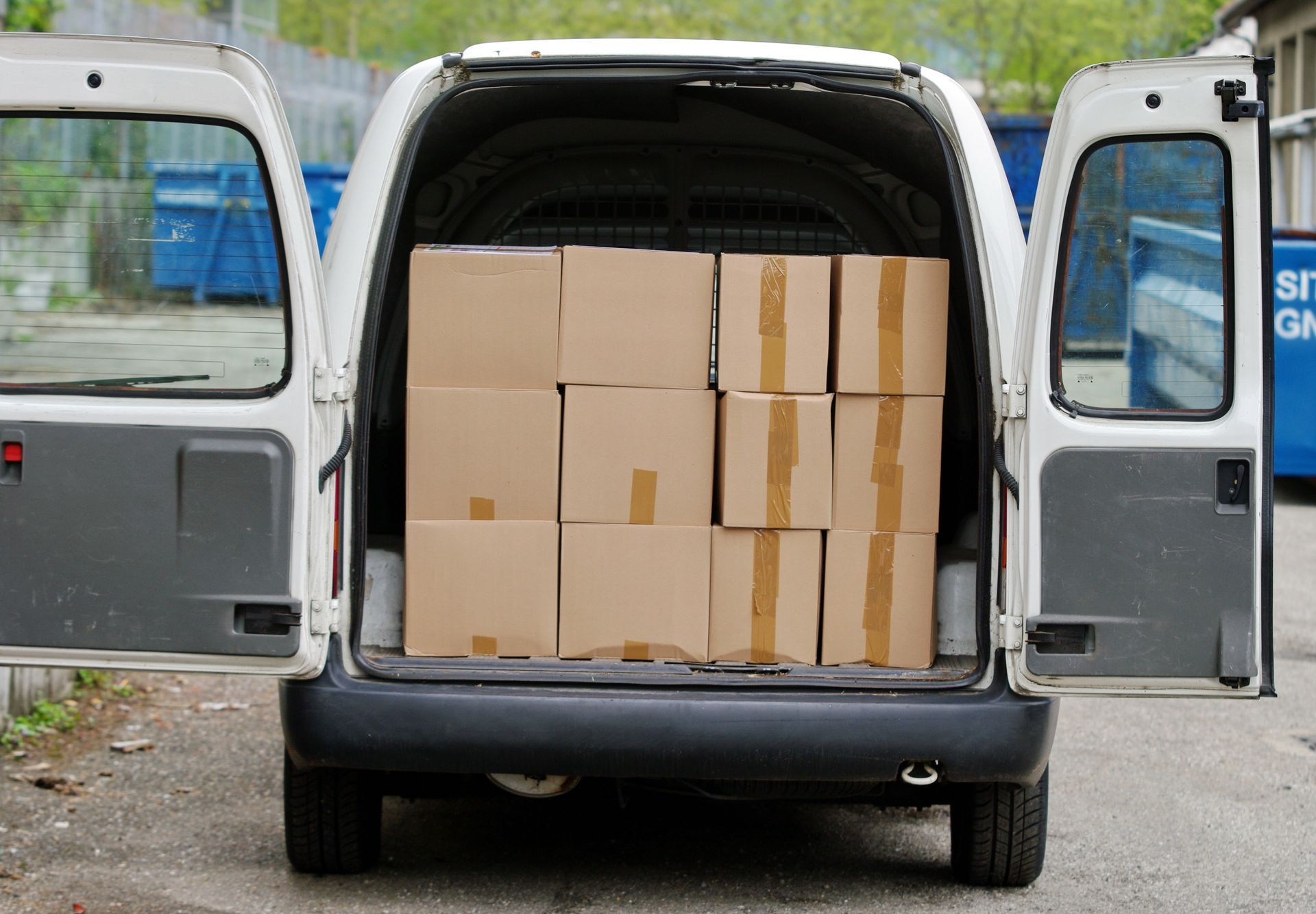 Vue arrière d'une camionnette de livraison blanche, portes ouvertes, révélant un espace de chargement rempli de cartons.