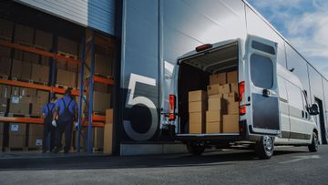 Véhicule transportant des colis avec les portes arrière ouvertes devant un entrepôt.
