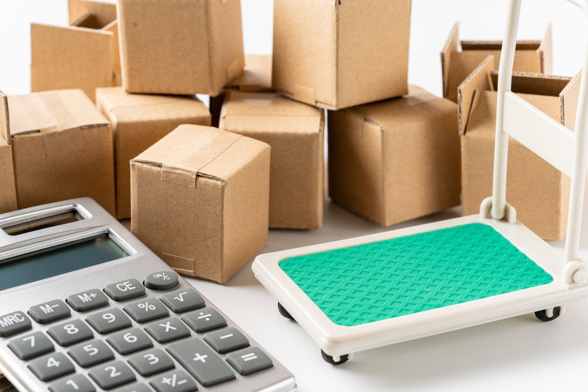 Une calculatrice à côté d'une petite balance numérique vide et de plusieurs boîtes en carton.