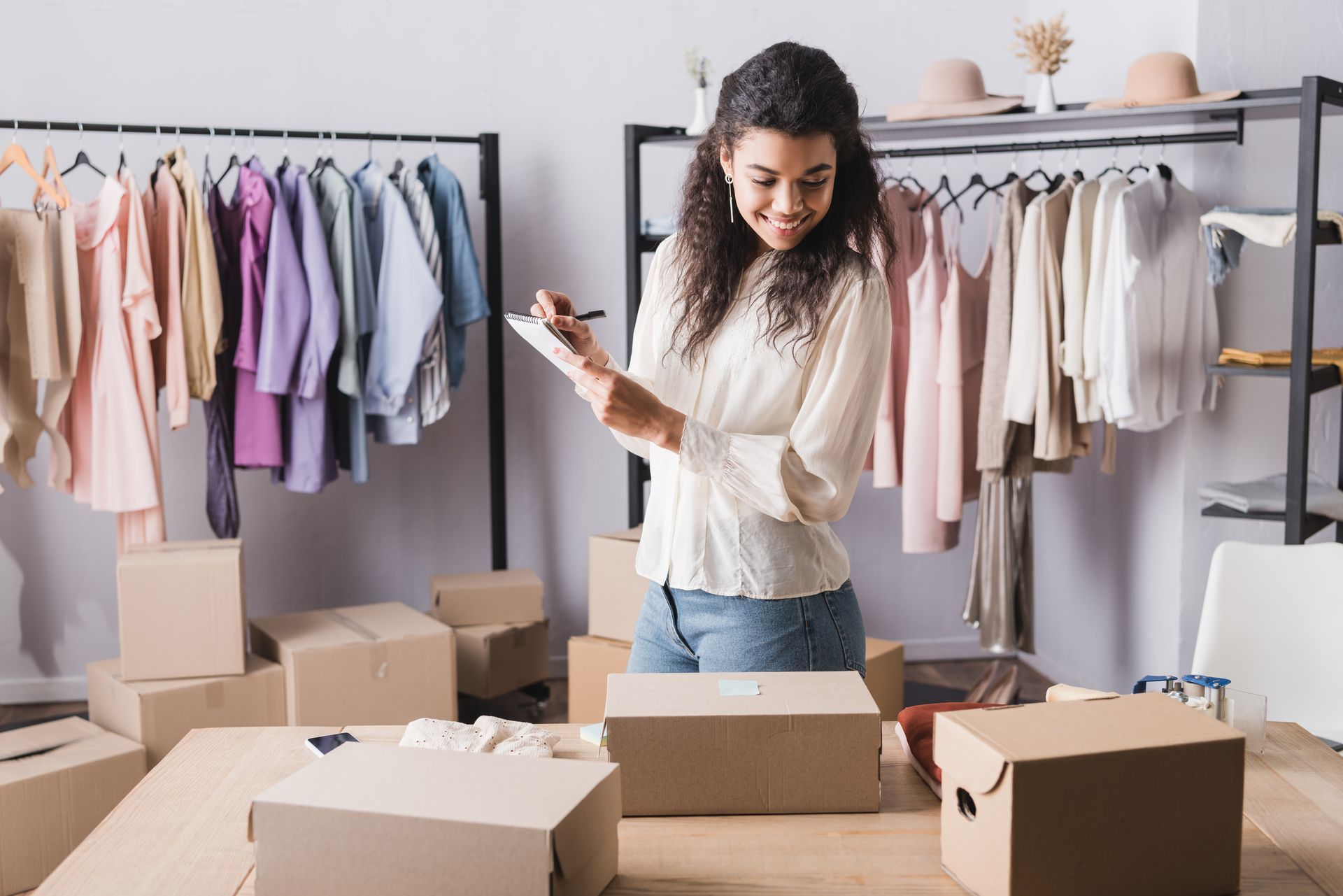 Une personne consulte une liste, parmi des portants de vêtements et des cartons dans une boutique.