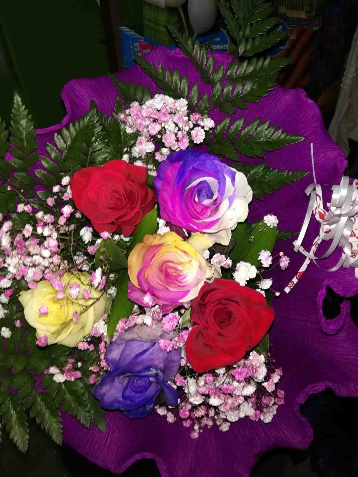 Un ramo de rosas de colores envuelto en papel morado.