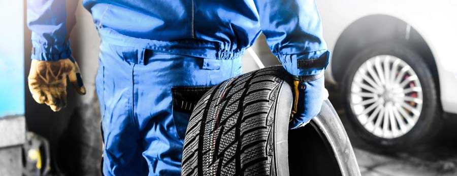 Un garagiste en bleu de travail qui tient un pneu dans sa main droite
