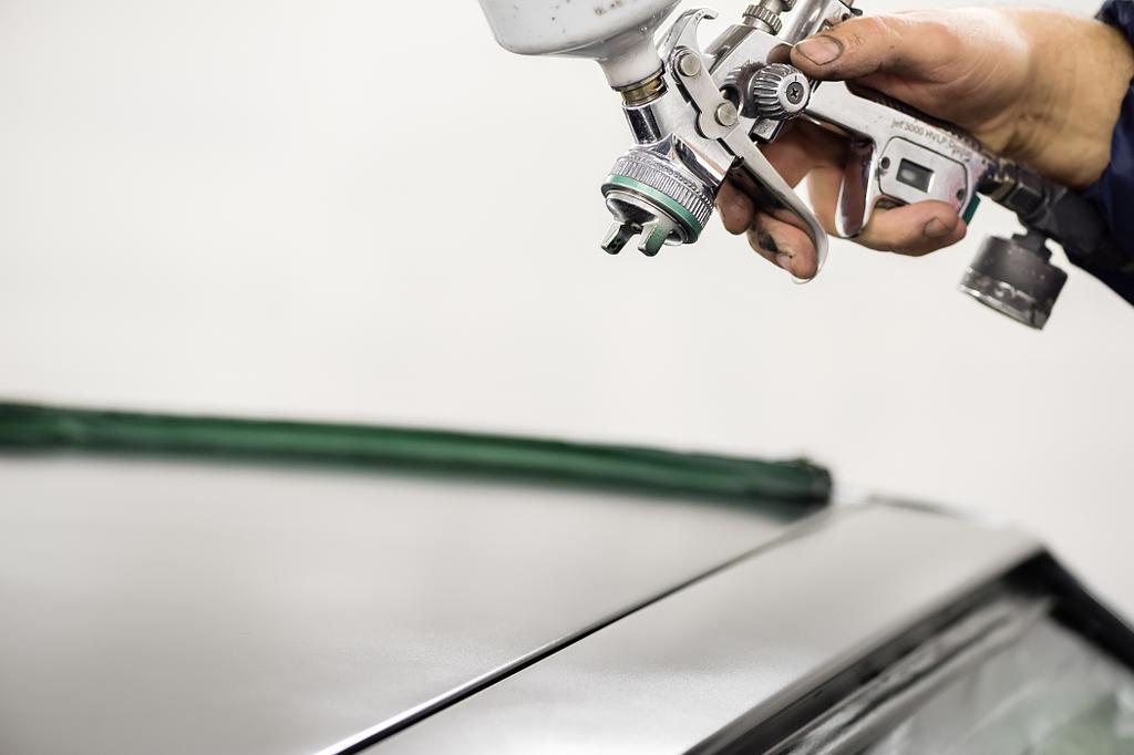 Main qui tient un pistolet à peinture au-dessus d'une voiture