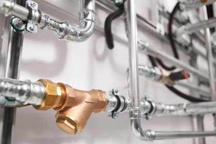 Primer plano de tuberías y accesorios de metal, incluido un filtro de latón, en una sala de máquinas.
