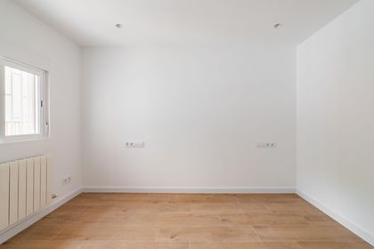 Habitación vacía con suelo de madera clara, paredes blancas y una ventana con radiador.