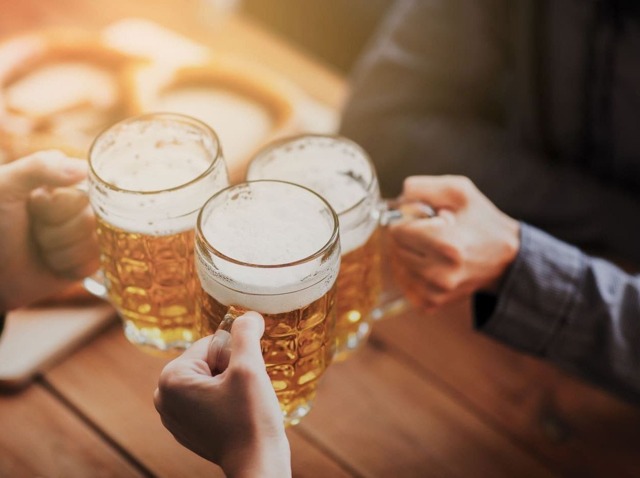 Un grupo de personas están brindando con jarras de cerveza en una mesa de madera.