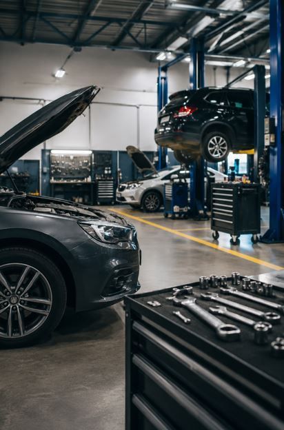 Taller mecánico con coches en elevadores y capó abierto, herramientas en primer plano