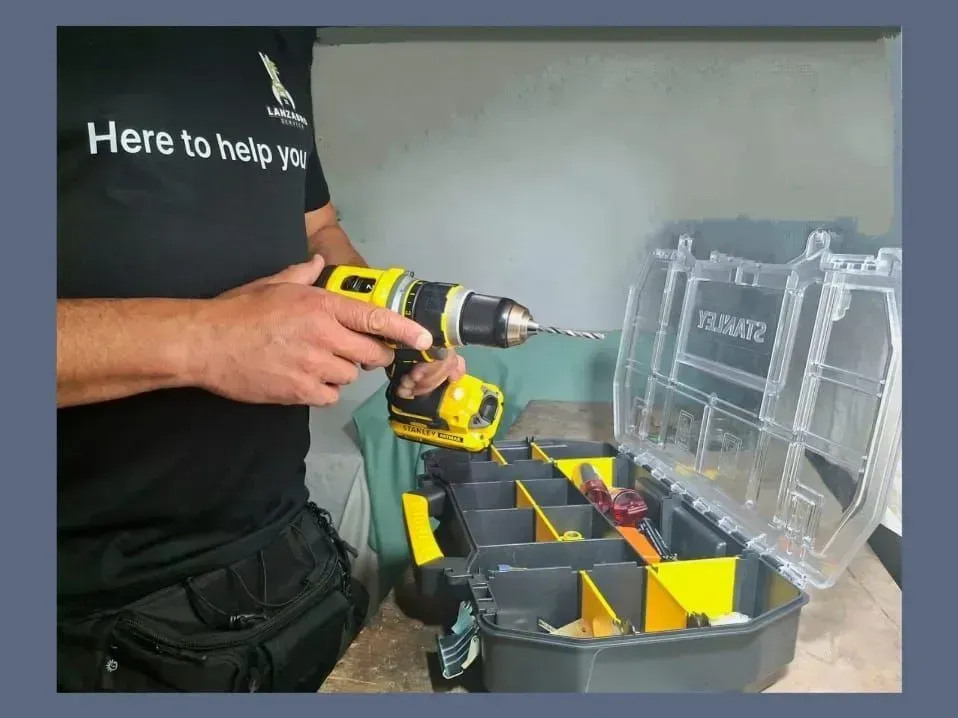 Una persona con una camisa negra sostiene un taladro inalámbrico amarillo y negro sobre un estuche organizador Stanley abierto.