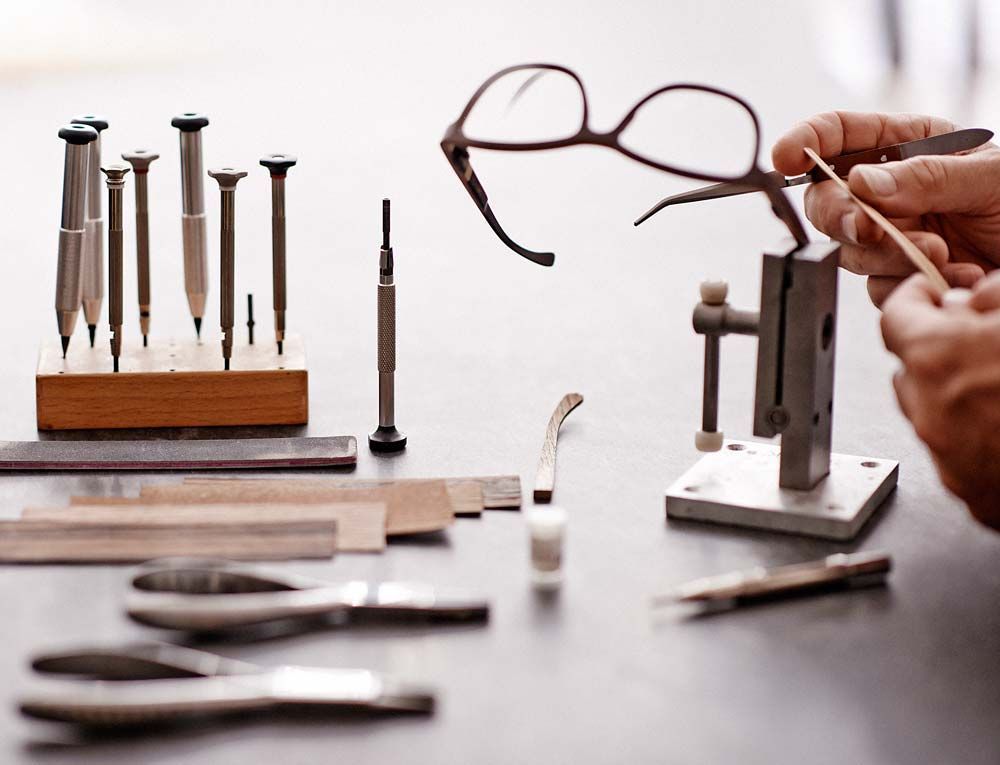 Personne réparant des lunettes avec des outils sur une table ; gros plan.