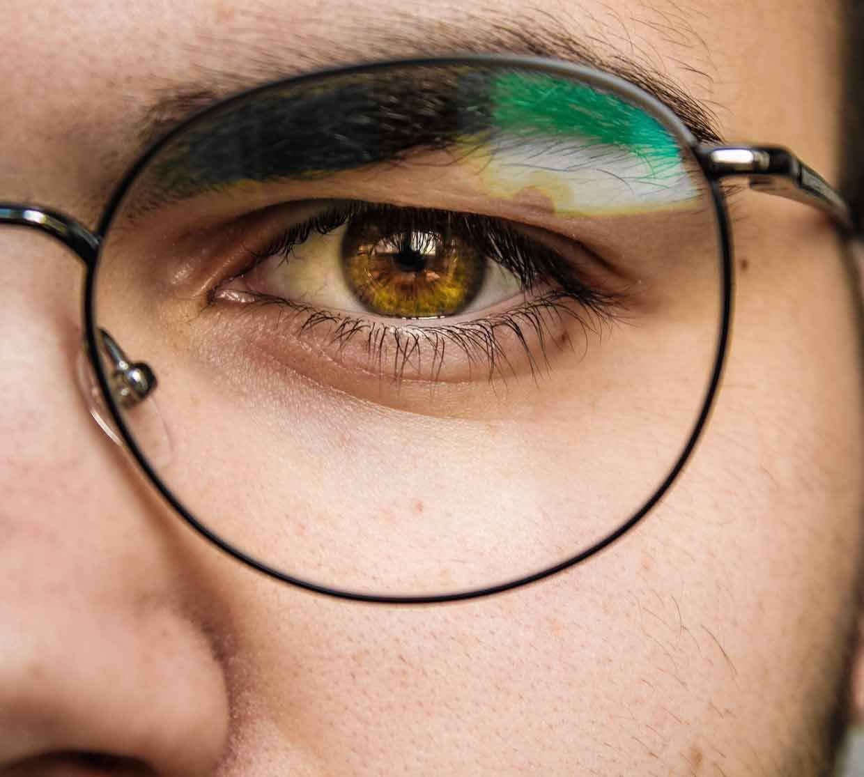 Gros plan de l'œil d'une personne, iris marron, portant des lunettes noires rondes.