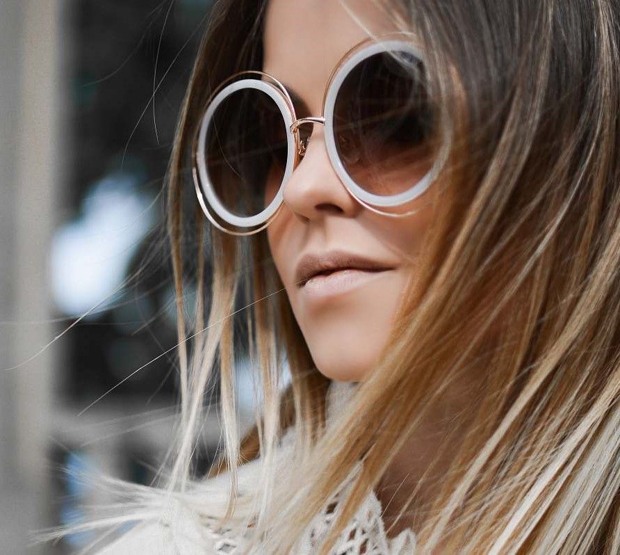 Femme portant de grandes lunettes de soleil rondes à monture blanche ; cheveux clairs, à l'extérieur.