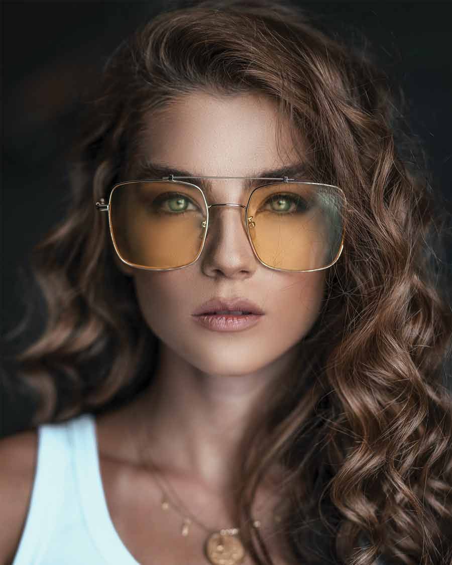 Femme aux cheveux bruns bouclés, portant des lunettes de soleil teintées jaunes, gros plan.