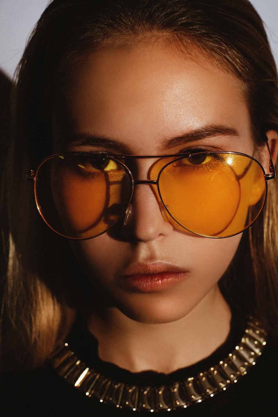Femme portant des lunettes de soleil jaunes et un collier en or, éclairage dramatique.