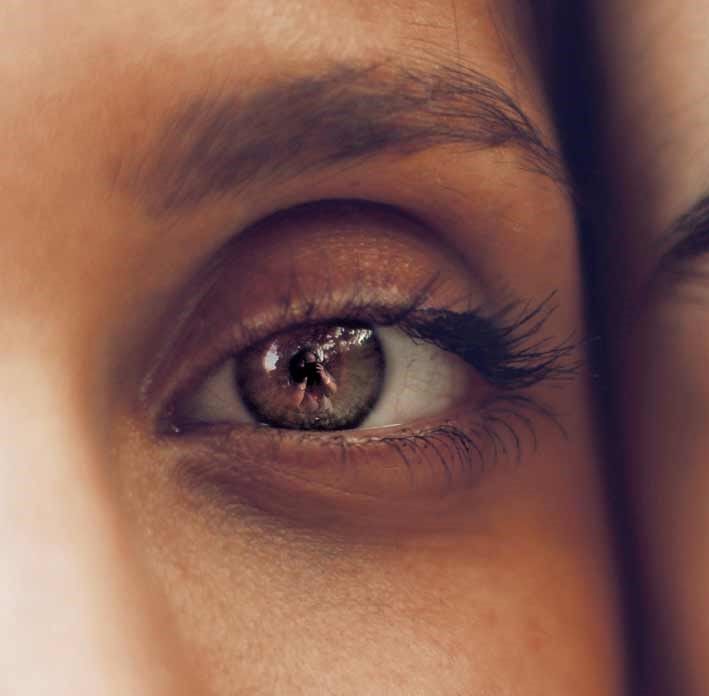 Gros plan sur un œil marron subtilement maquillé. Regard droit. Lumière tamisée.