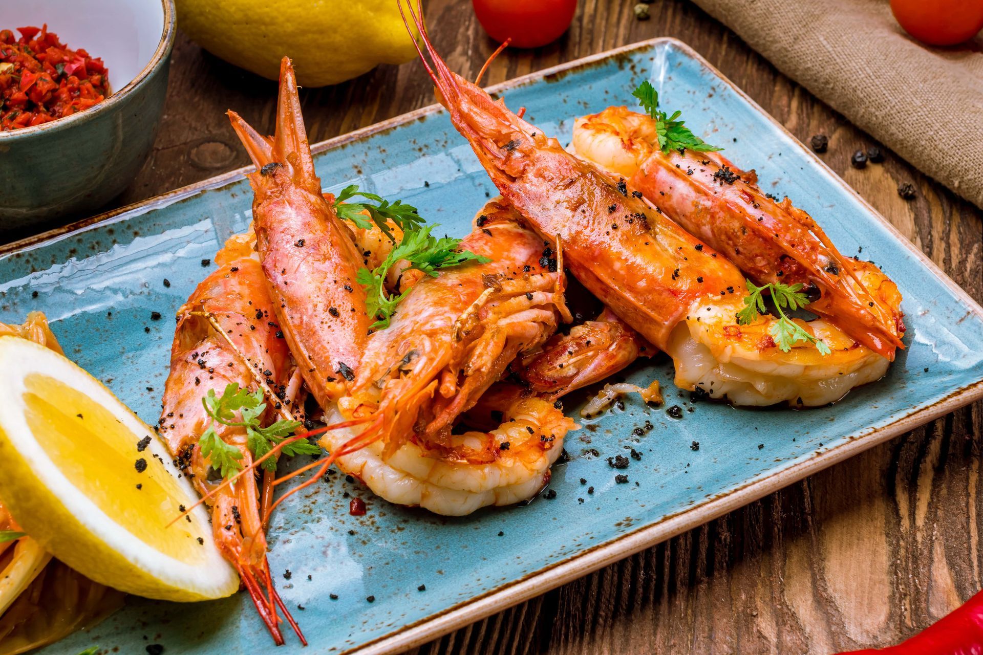 Brochettes de crevettes grillées sur une assiette bleue avec des quartiers de citron et des herbes sur une table rustique