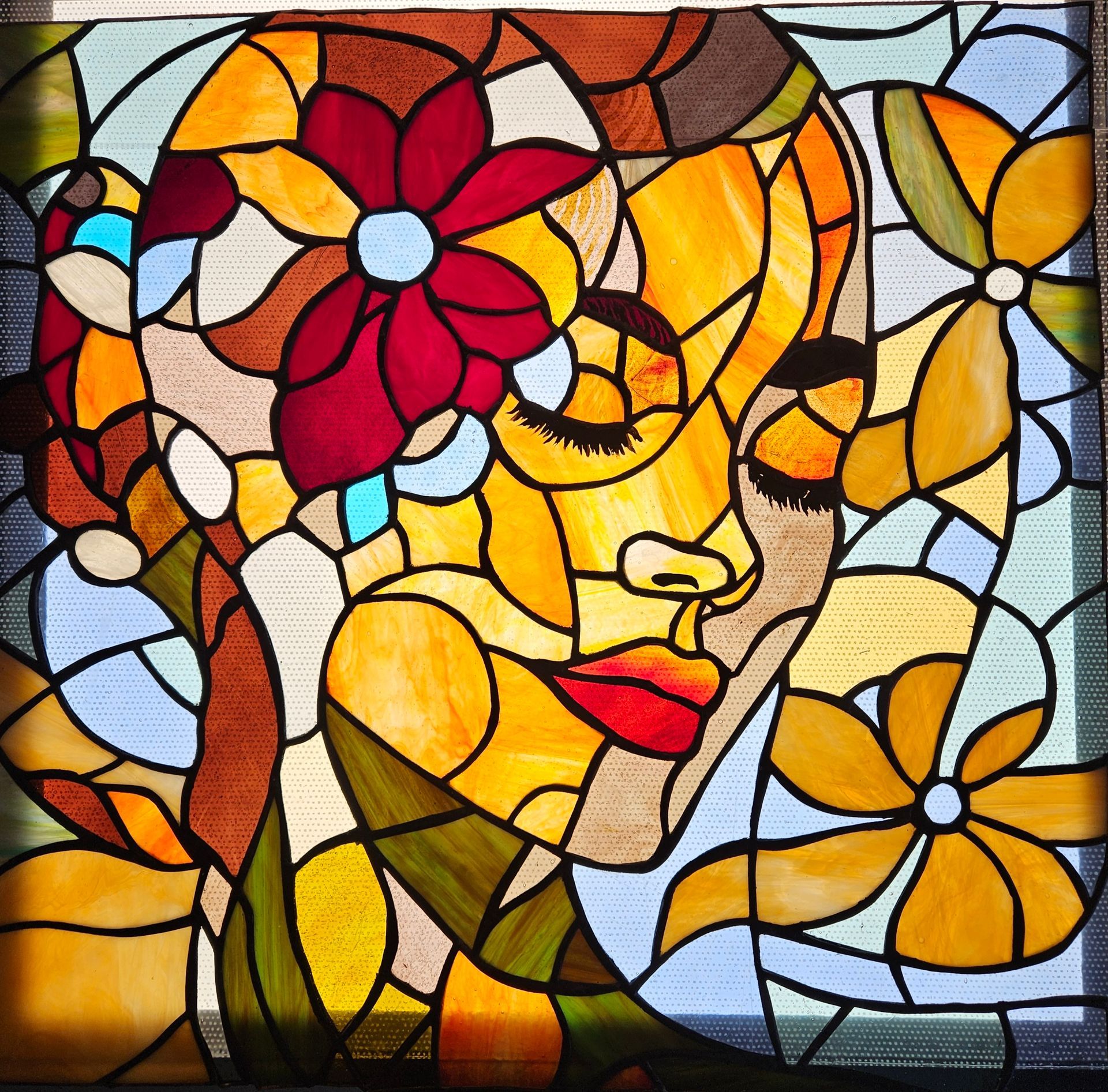 Una mujer está de pie junto a una pintura de vitral del rostro de una mujer.