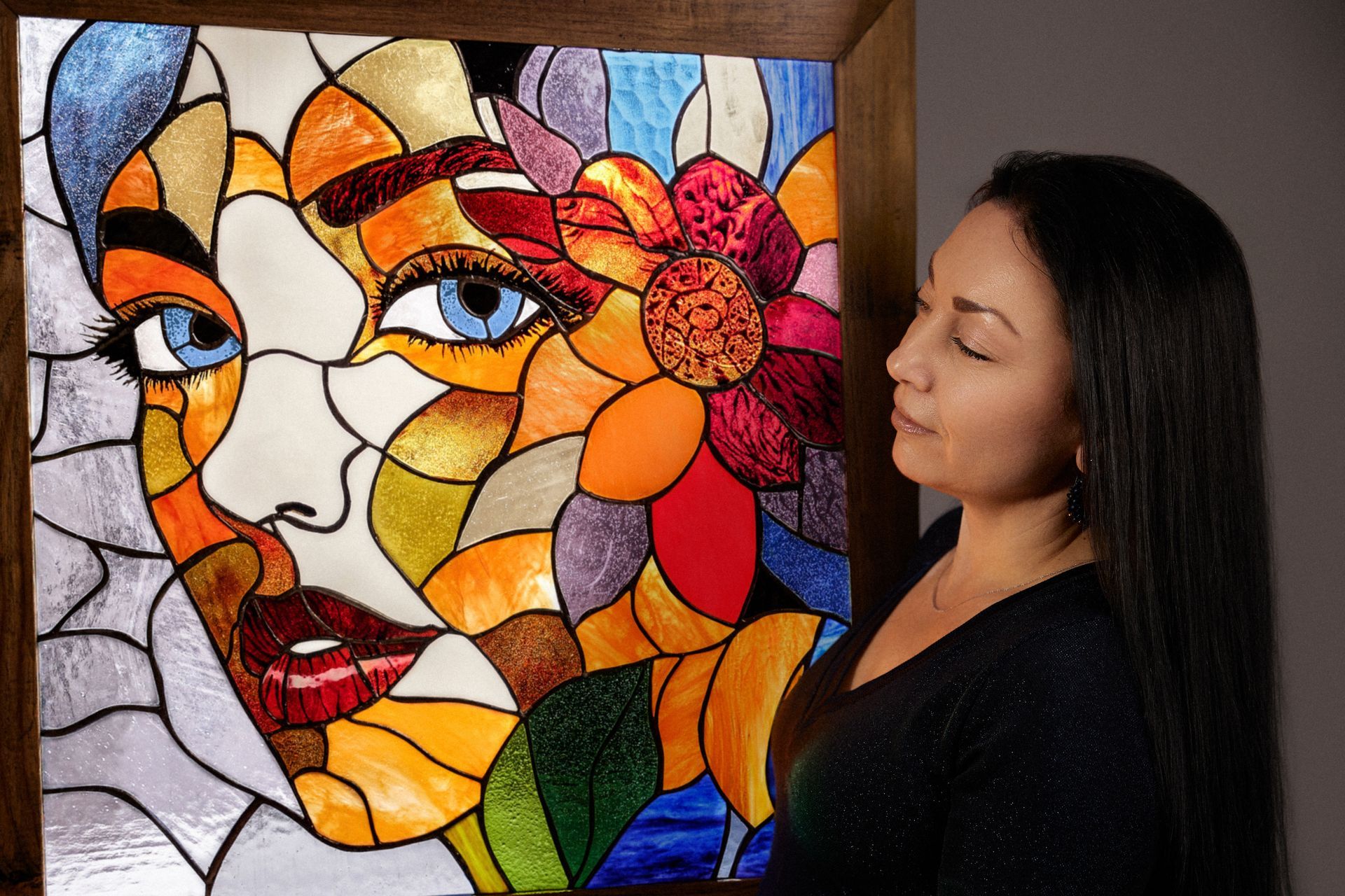 Una mujer está de pie junto a una pintura de vitral del rostro de una mujer.