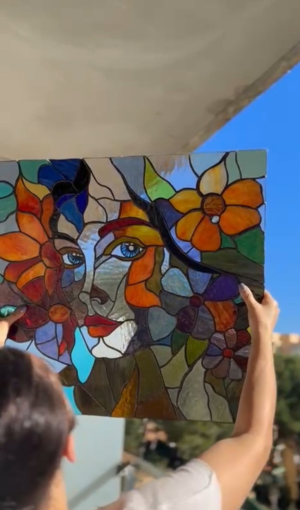 Una persona sostiene una pintura de vidriera del rostro de una mujer y flores.