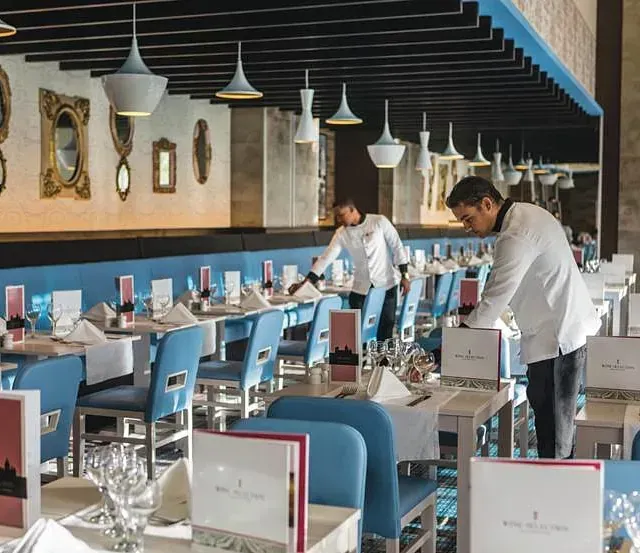 Un hombre con una chaqueta blanca está poniendo mesas en un restaurante.