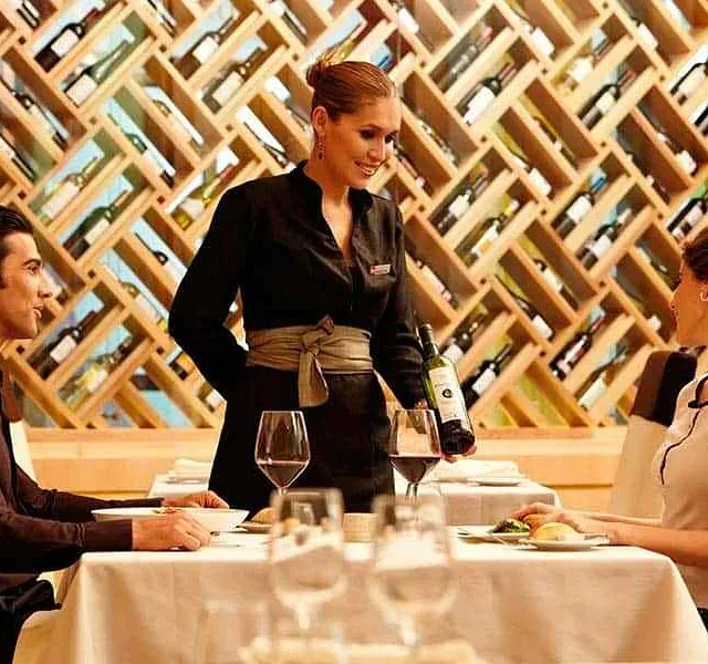 Una mujer está sirviendo vino a un hombre y a una mujer en un restaurante.