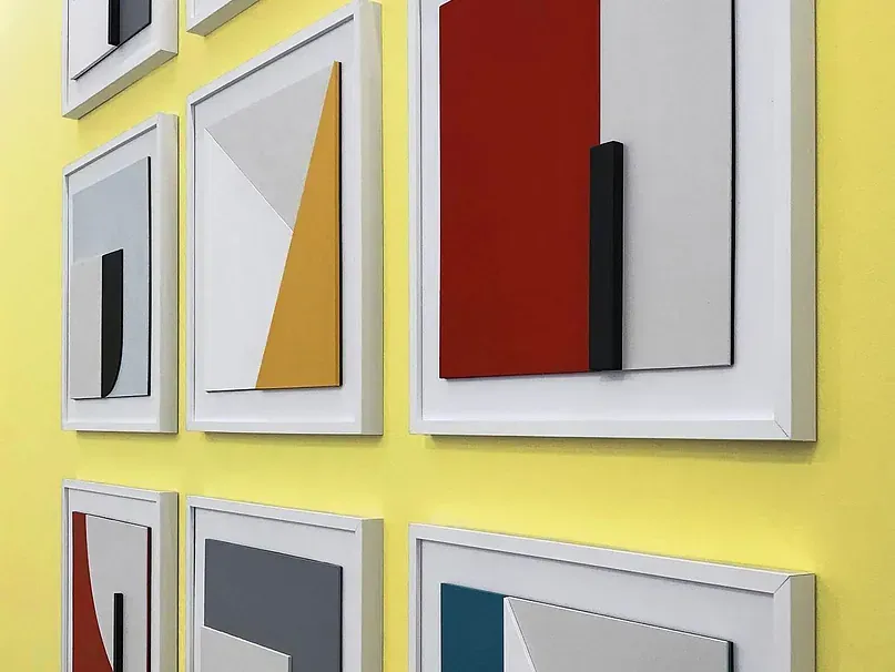 Un grupo de cuadros cuelgan en una pared amarilla.