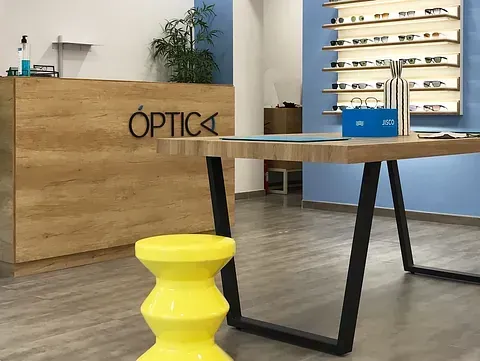 Un taburete amarillo está junto a una mesa de madera en una tienda de óptica.
