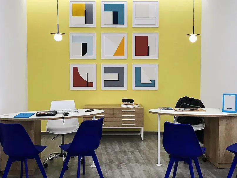 Una habitación con una pared amarilla y sillas y mesas azules.