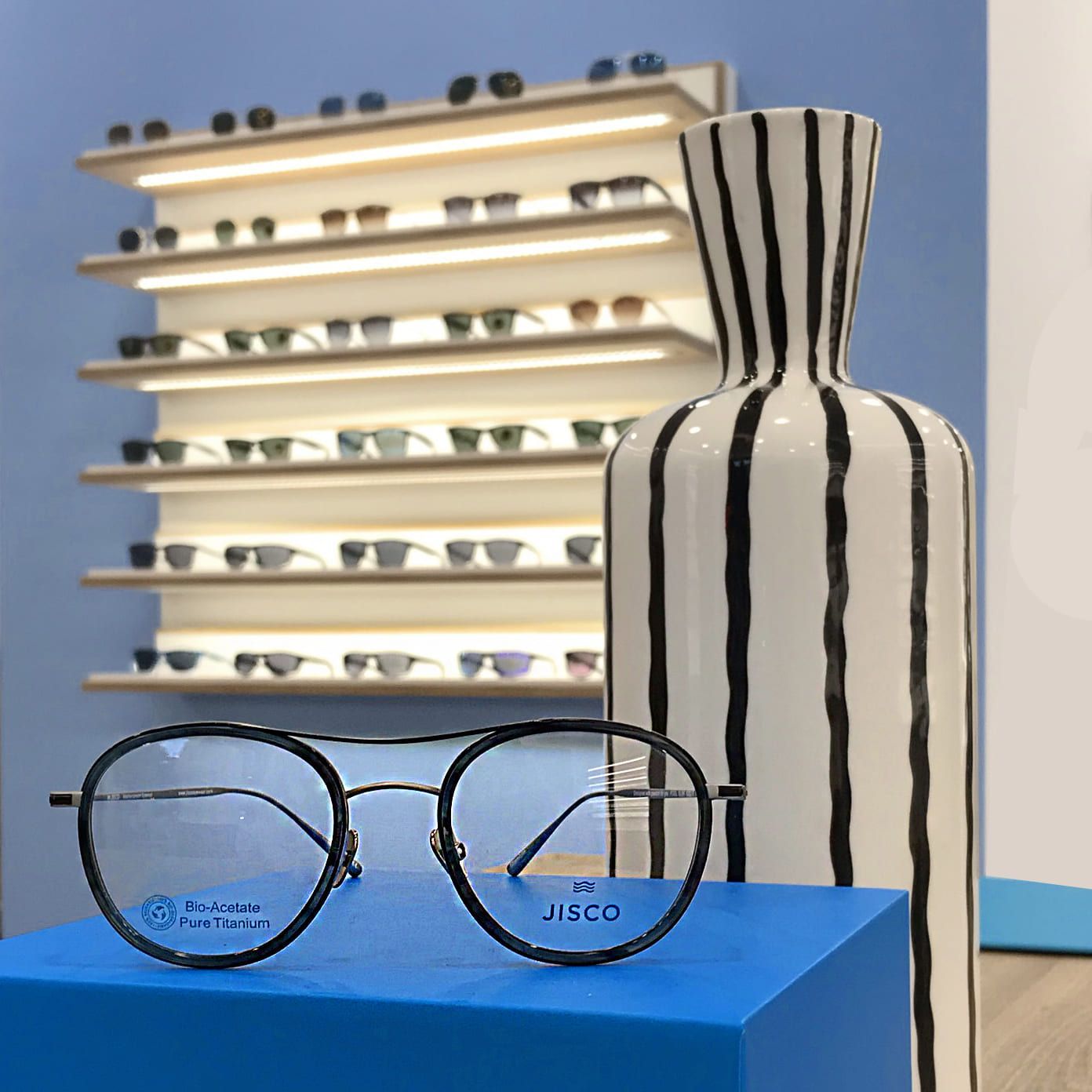 Un par de gafas encima de una caja azul al lado de un jarrón de rayas.