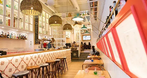 Un restaurante con mesas y taburetes y un bar.