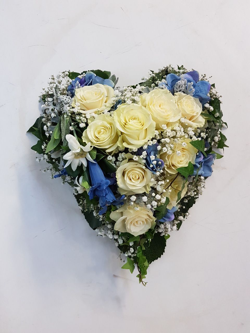 Herz aus weißen Rosen und blauen Blumen