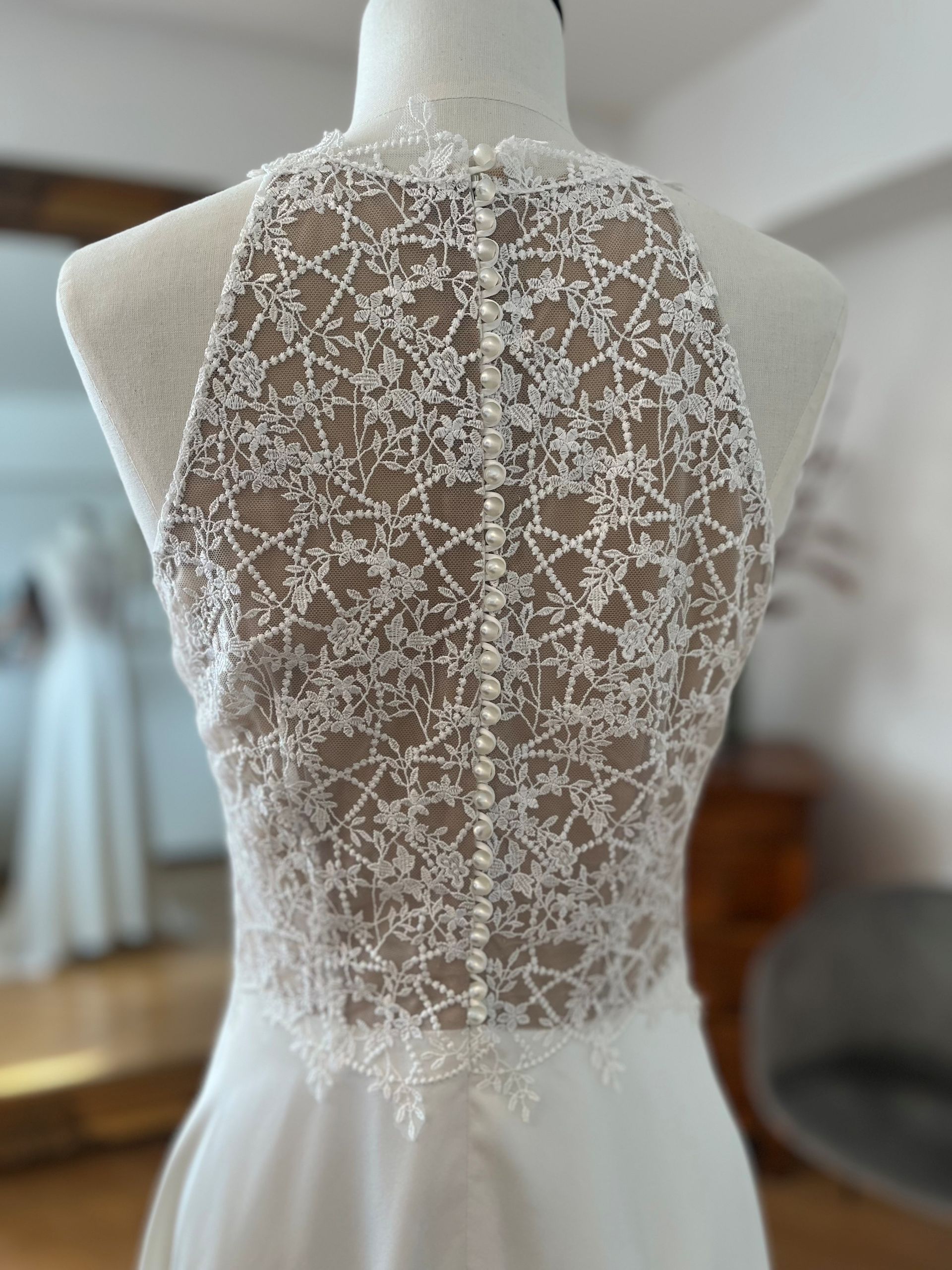 Weißes Spitzenkleid mit floralem Lochmuster und tiefem, transparentem Rückenausschnitt an einer Schaufensterpuppe