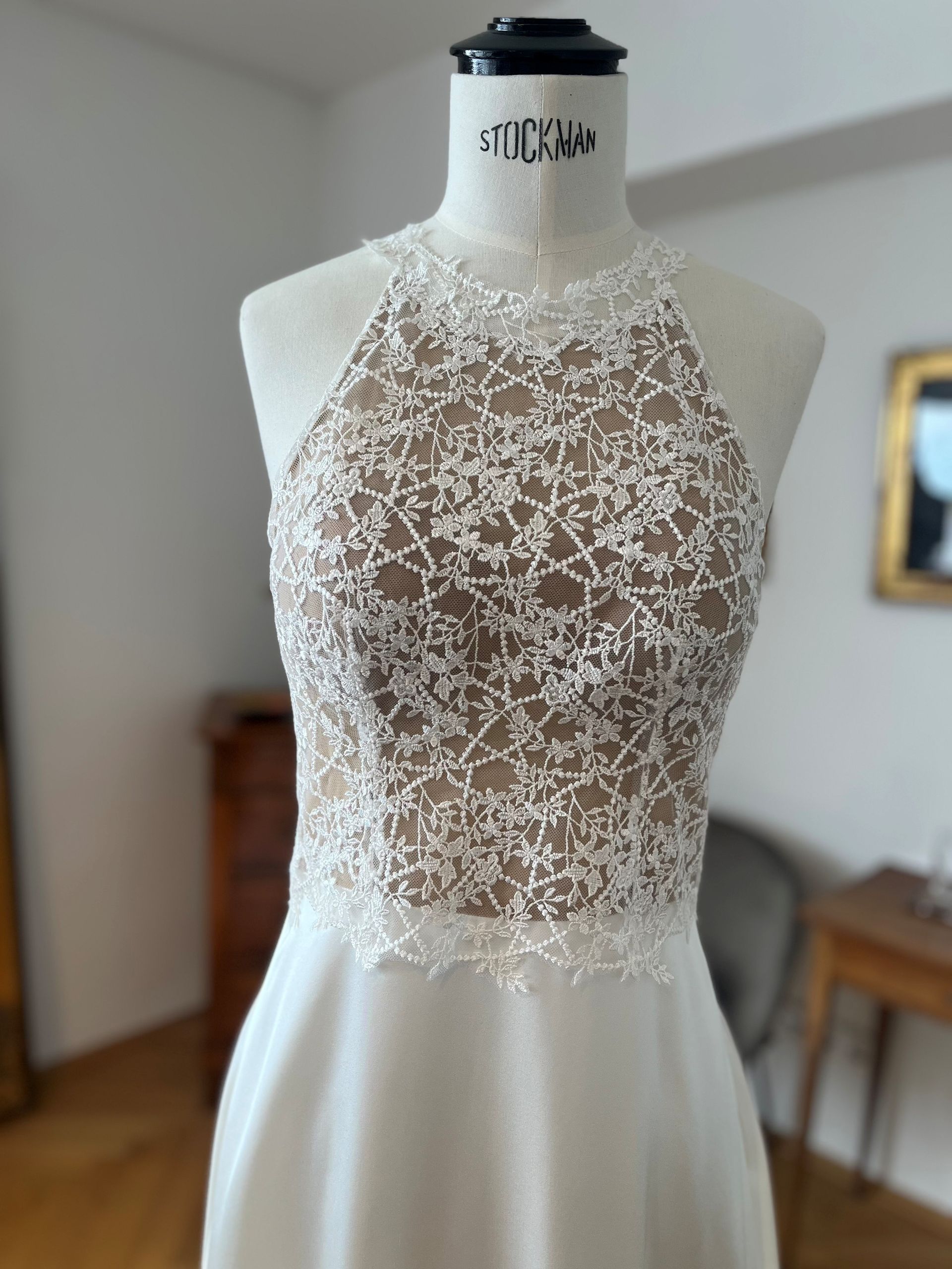Elfenbeinfarbenes Brautkleid mit Neckholder aus Spitze an einer Schaufensterpuppe in einem sanft beleuchteten Raum