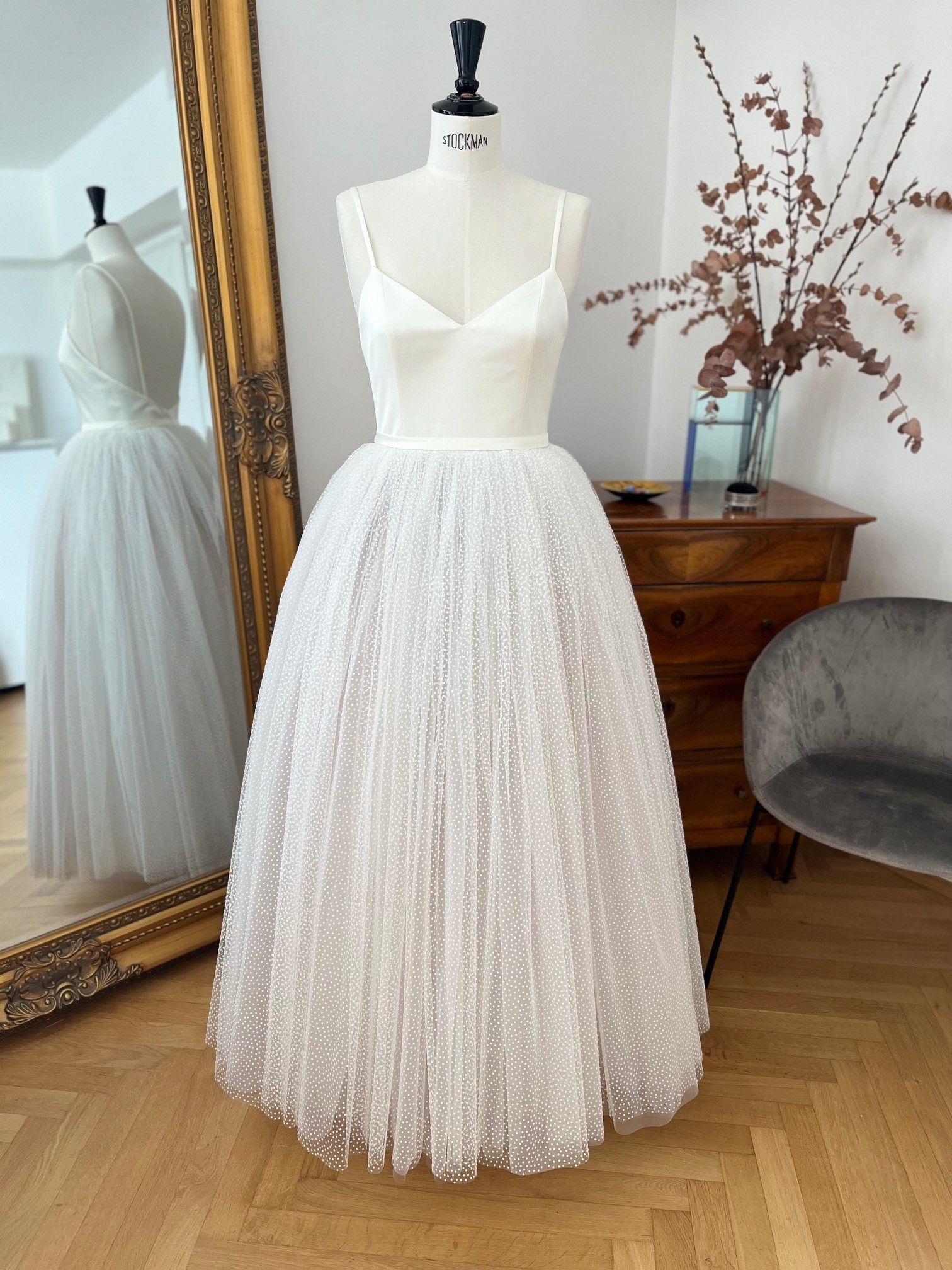 Weißes, ärmelloses Kleid an einer Schaufensterpuppe in einem hellen Raum, in dem sich das Kleid in einem Spiegel reflektiert.