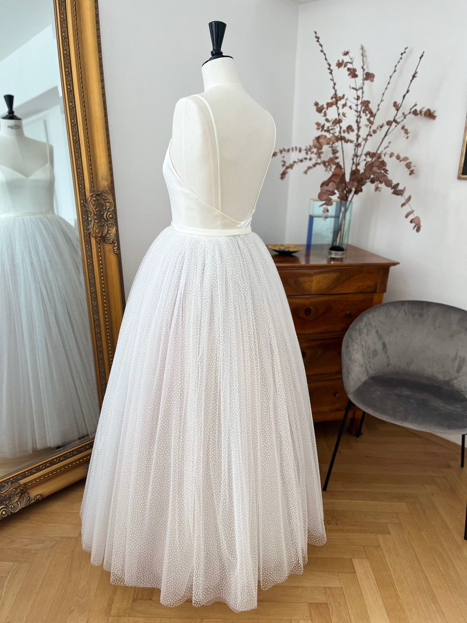 Weißes, perlenbesetztes, trägerloses Kleid an einer Schaufensterpuppe in einem Raum mit Spiegel, Kommode und Stuhl
