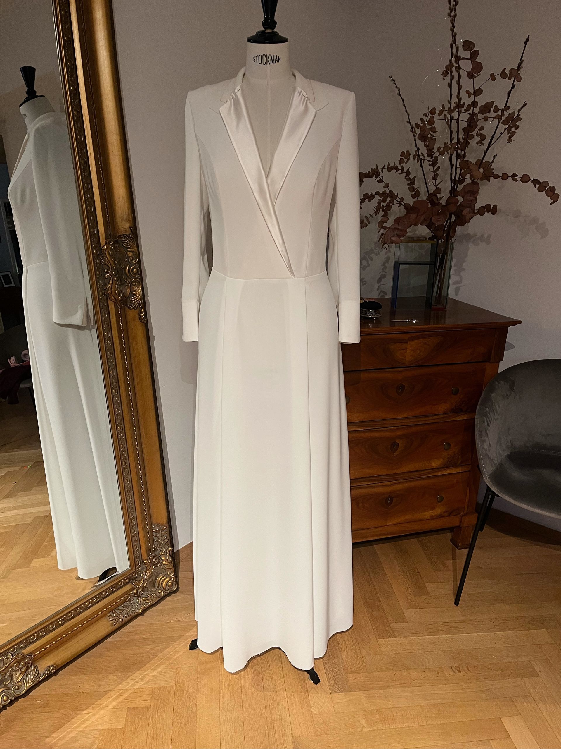Weißes, langärmeliges Wickelkleid an einer Schaufensterpuppe neben einem Ganzkörperspiegel und einer Holzkommode.