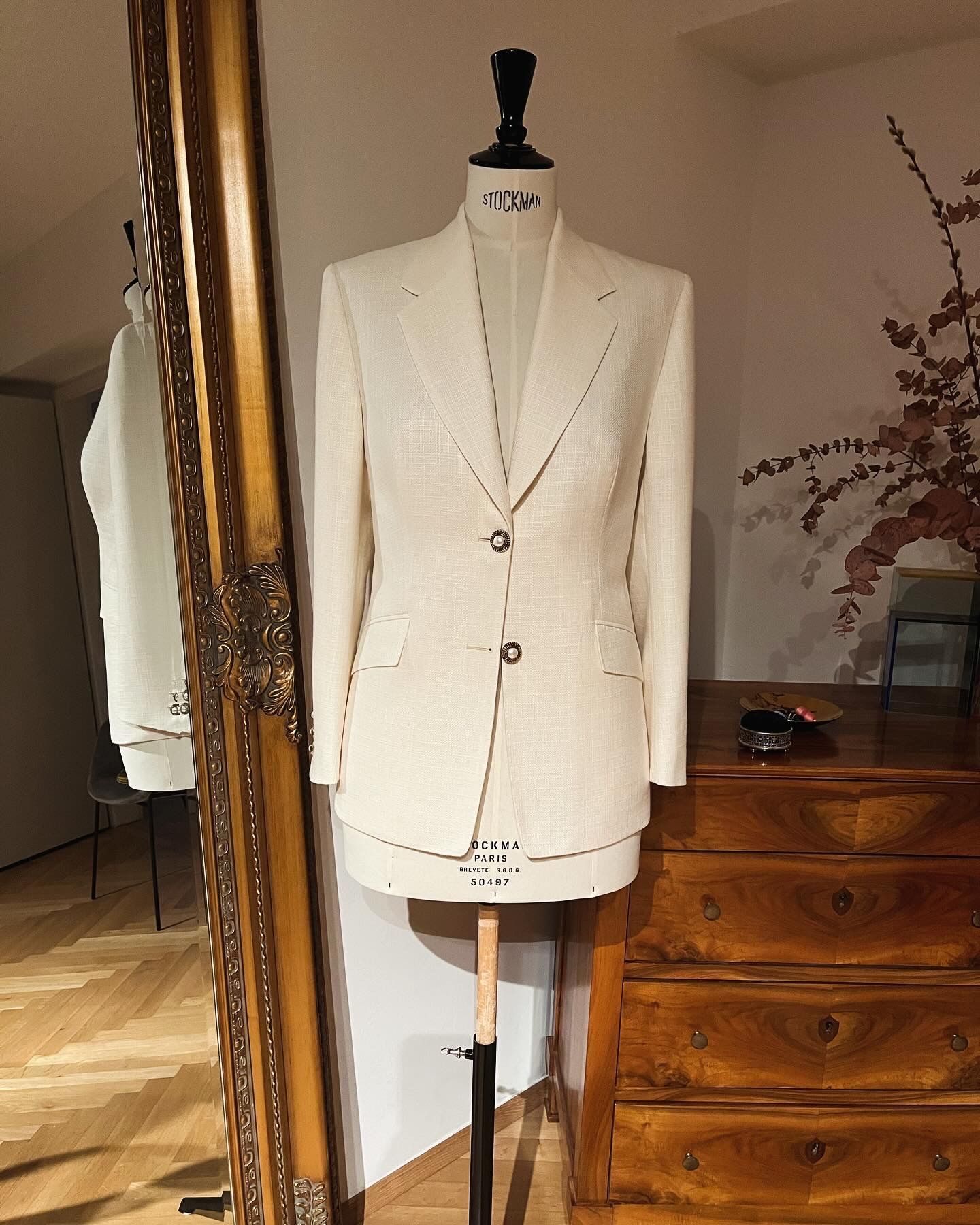 Ein cremefarbener Blazer auf einer Schaufensterpuppe neben einer Holzkommode und einem großen Spiegel in einem Schlafzimmer.