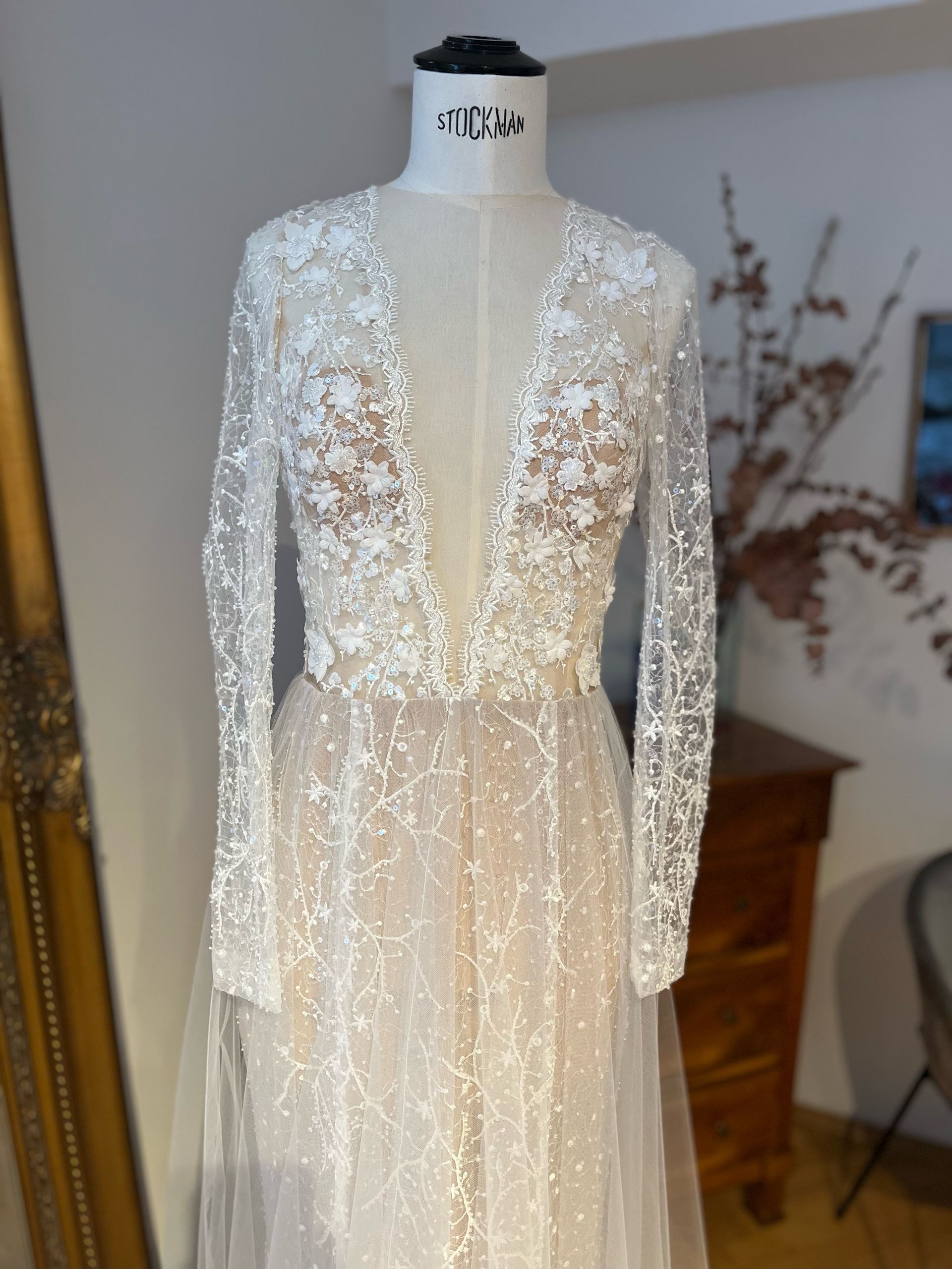 Perlenbesetztes, durchsichtiges, weißes Langarmkleid an einer Schaufensterpuppe in einem Zimmer