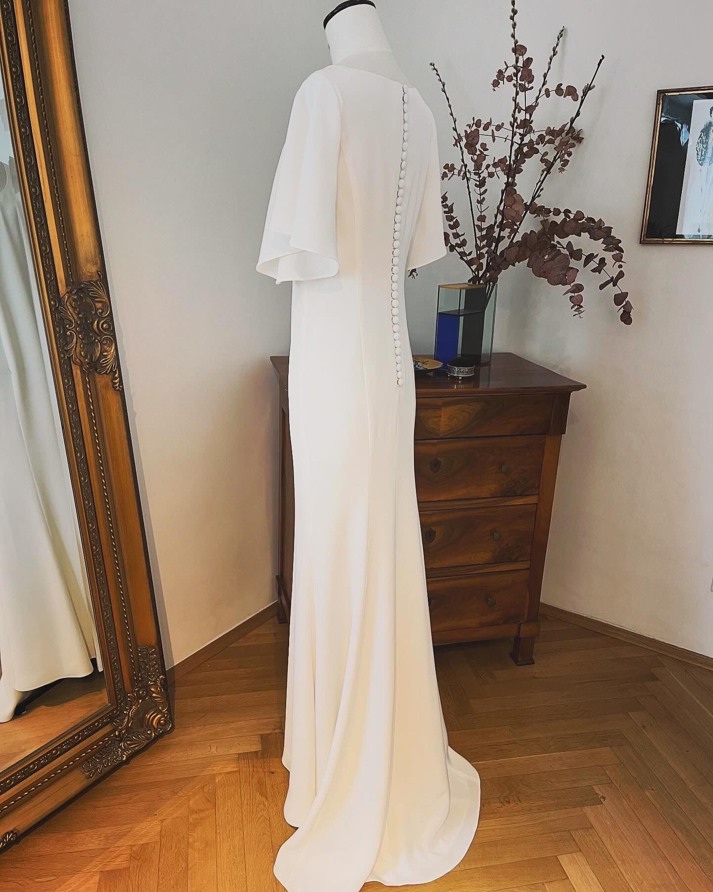 Weißes Kleid auf einer Schaufensterpuppe in einem Zimmer mit Holzboden, Spiegel und Kommode mit Vase mit Zweigen