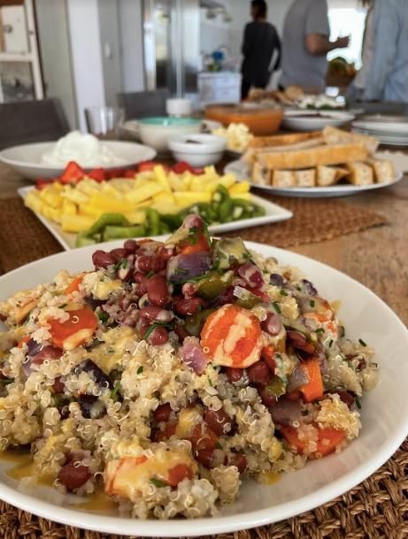 Ensalada de quinoa con verduras en un plato, rodeada de una serie de aperitivos sobre una mesa.