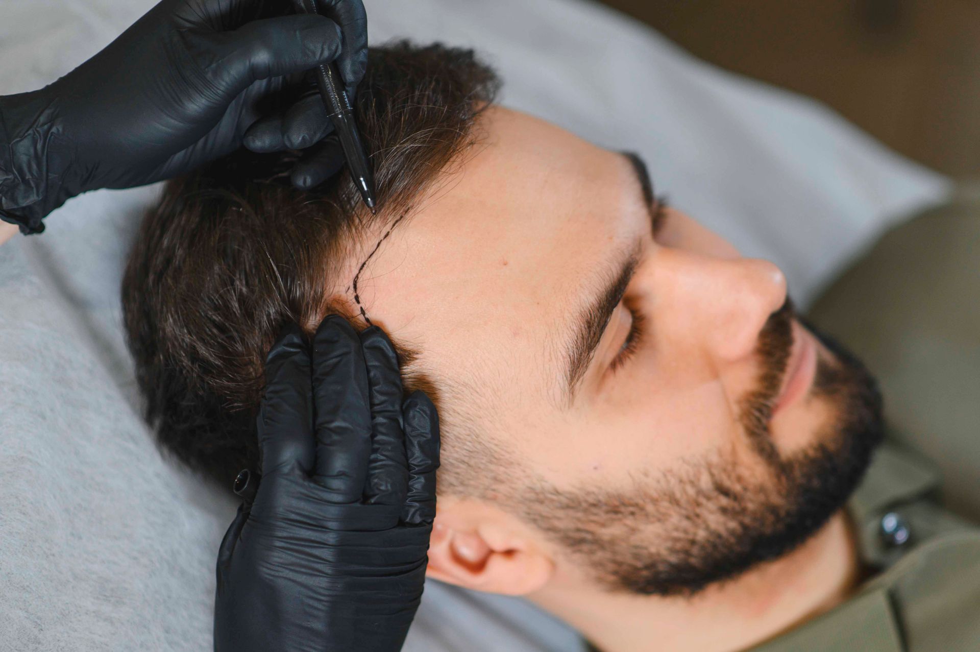 Schwarz behandschuhte Hände pflegen das Haar eines bärtigen Mannes, während er mit geschlossenen Augen zurückgelehnt liegt.